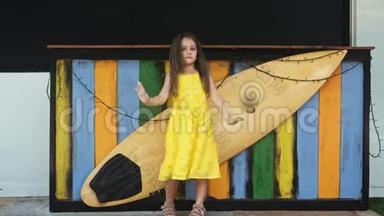 穿着黄色衣服的小美女站在冲浪板旁边